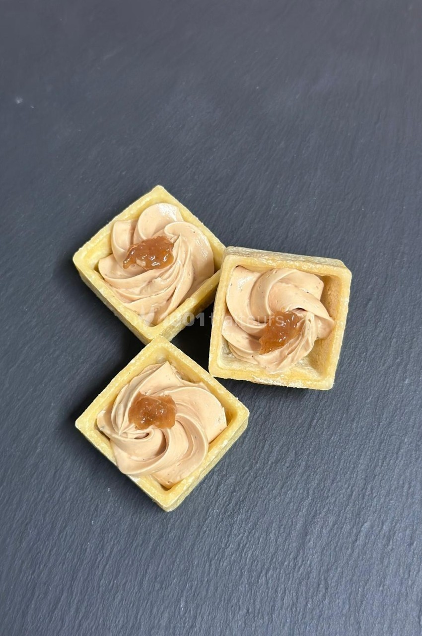 Tartelettes carrées garnies de crème beige et décorées d'une touche de caramel, posées sur une surface ardoisée.