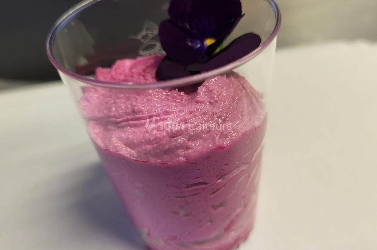 Mousse rose servie dans un verre transparent, décorée d'une fleur violette sur le dessus.