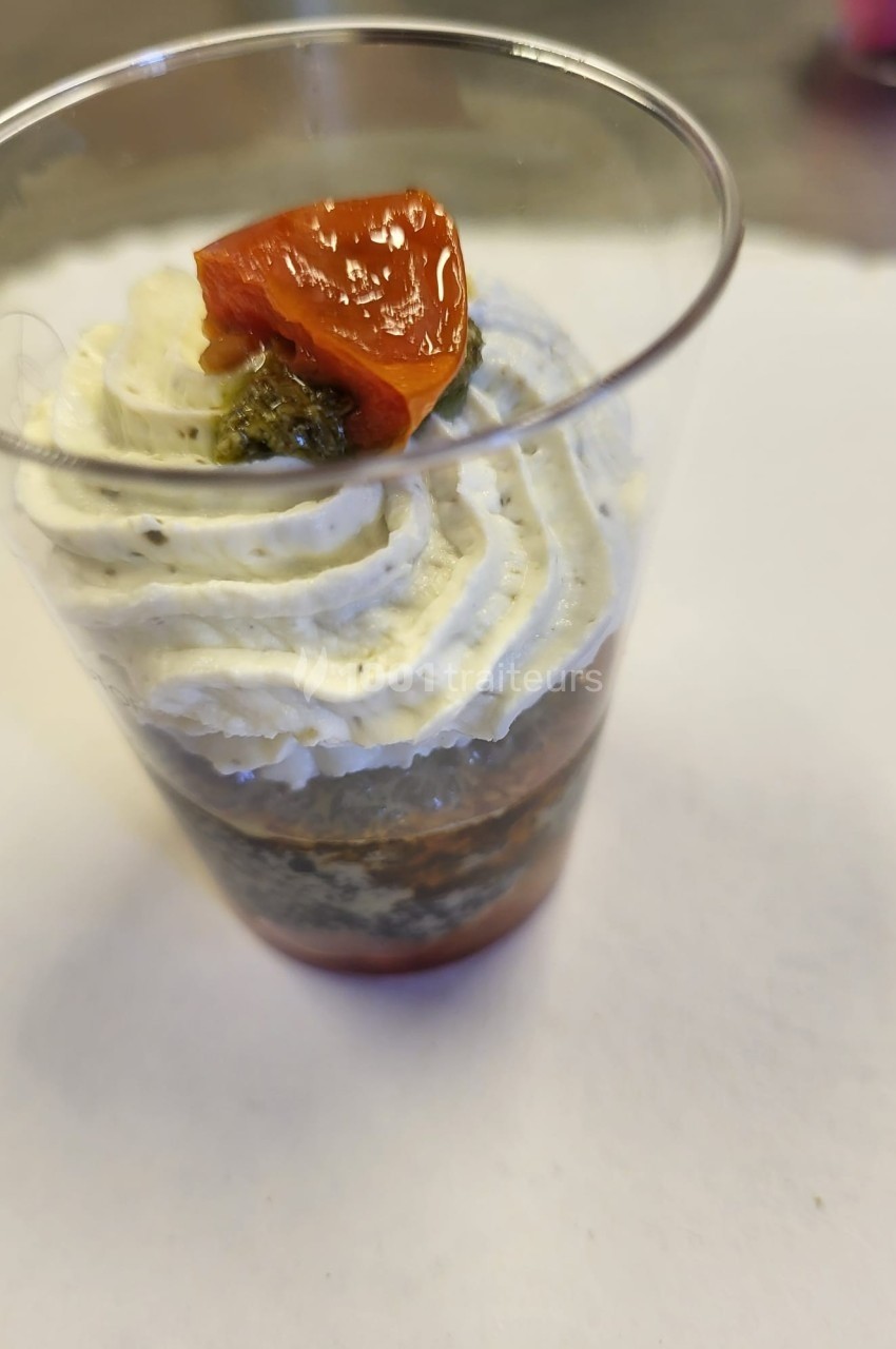 Verrine composée de couches de crème, tapenade et tomate confite, présentée sur une surface blanche.