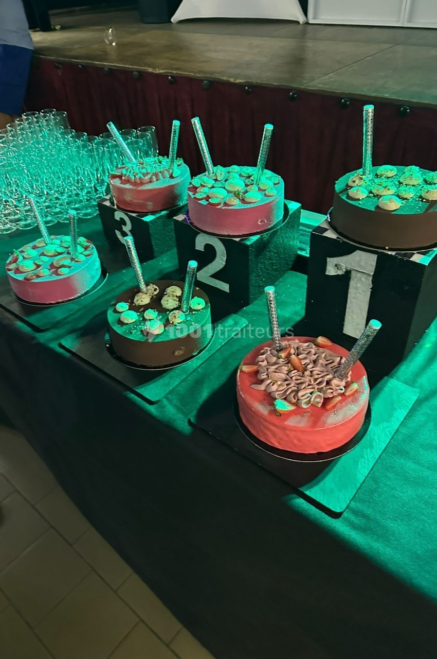 Des gâteaux décorés sont disposés sur des podiums numérotés, entourés de verres en arrière-plan.