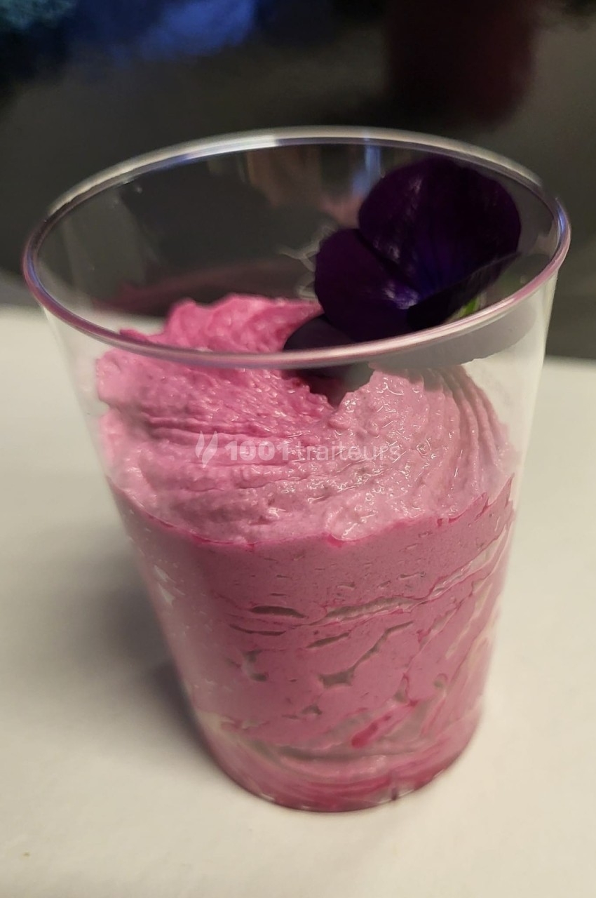 Mousse rose servie dans un verre transparent, décorée d'une fleur violette sur le dessus.