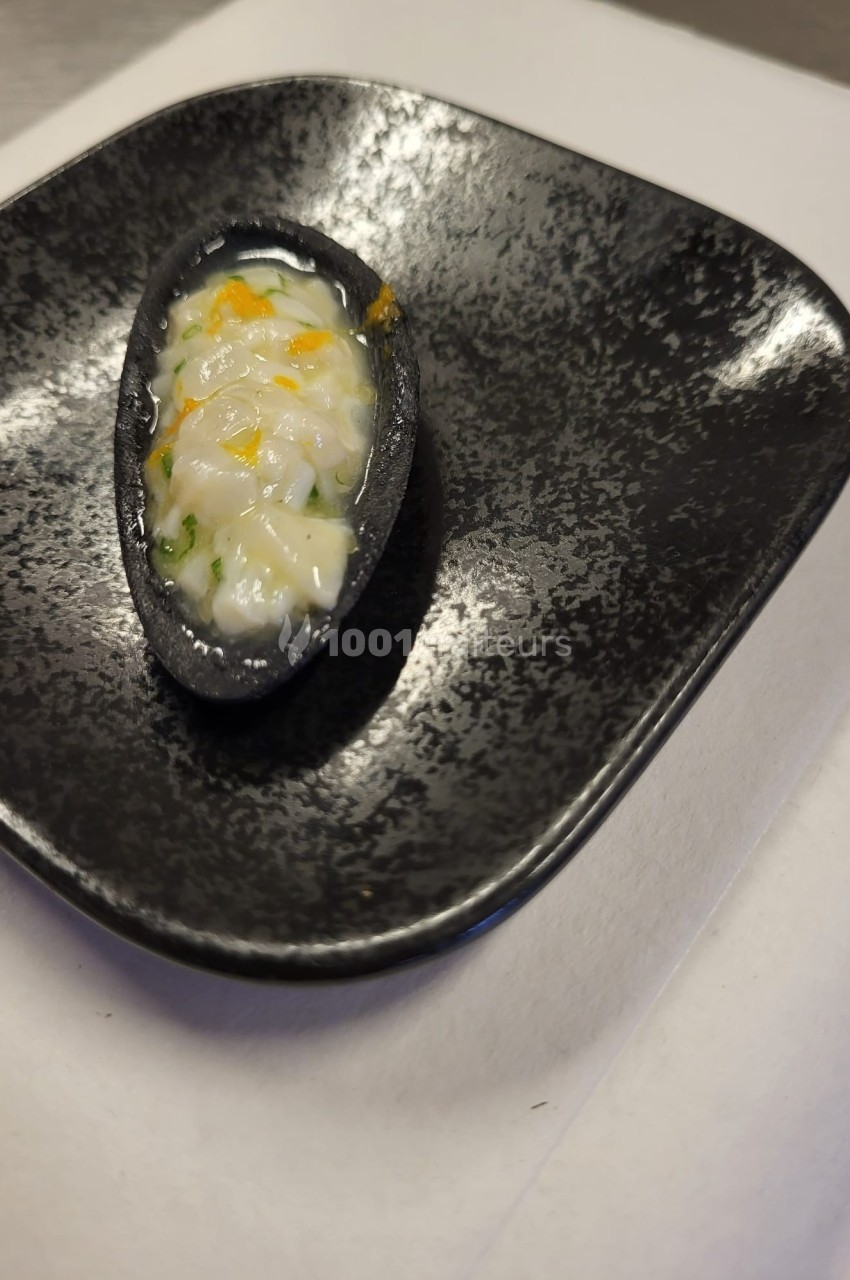 Bouchée servie dans une coque noire, garnie d'une préparation crémeuse avec des touches de jaune et de vert.