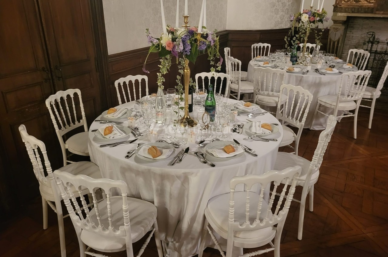 Tables rondes élégamment dressées avec nappes blanches, chaises assorties et centres de table fleuris dans une salle…