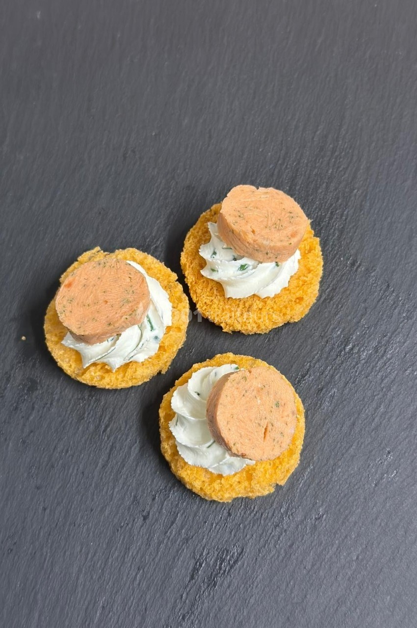 Trois amuse-bouches sur ardoise, composés de crackers, fromage frais et rondelles de terrine.