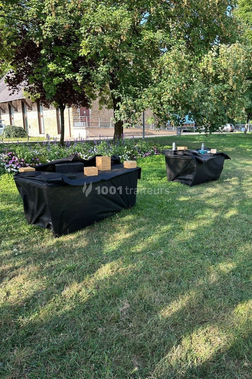 Deux tables recouvertes de nappes noires avec des objets en bois et des accessoires, installées dans un parc verdoyant.