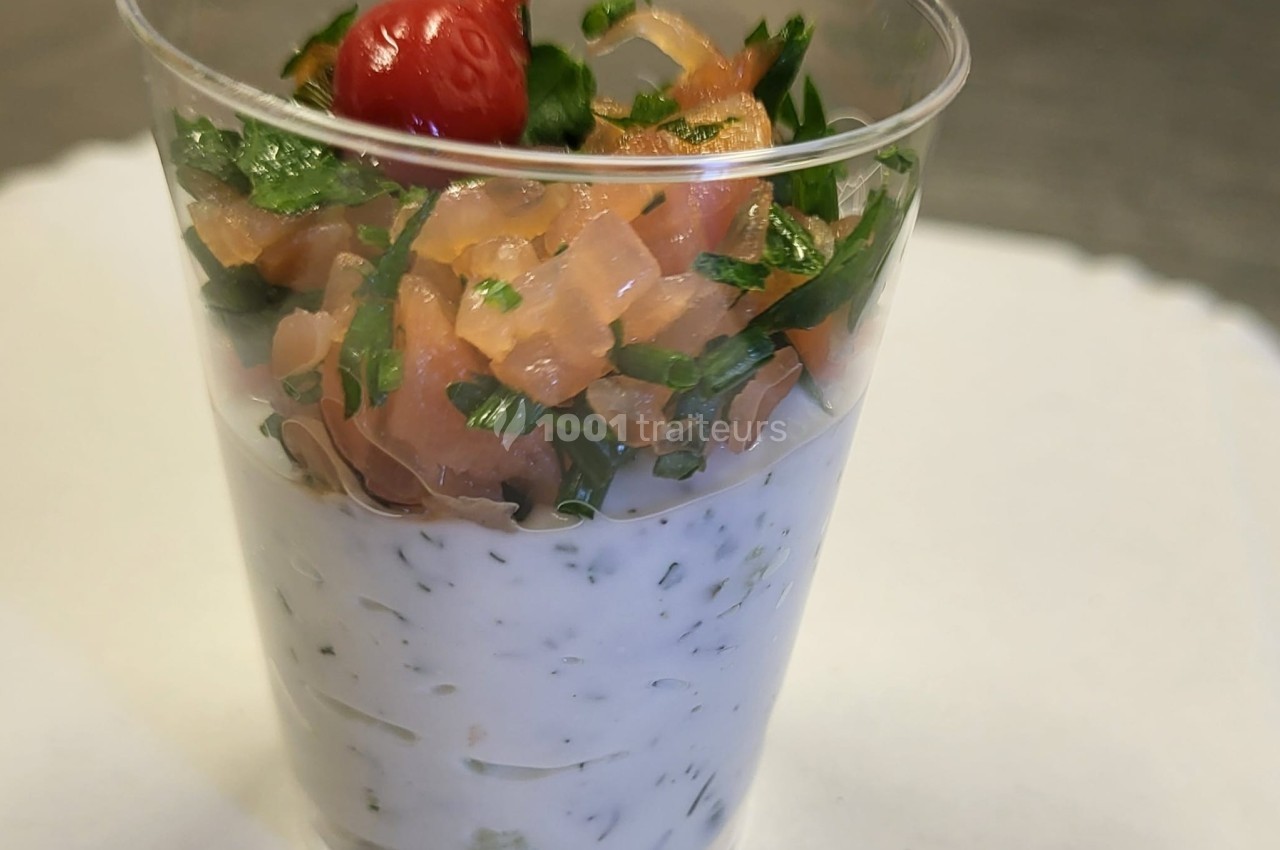 Verrine composée de crème aux herbes, dés de saumon fumé, persil et une tomate cerise en garniture.