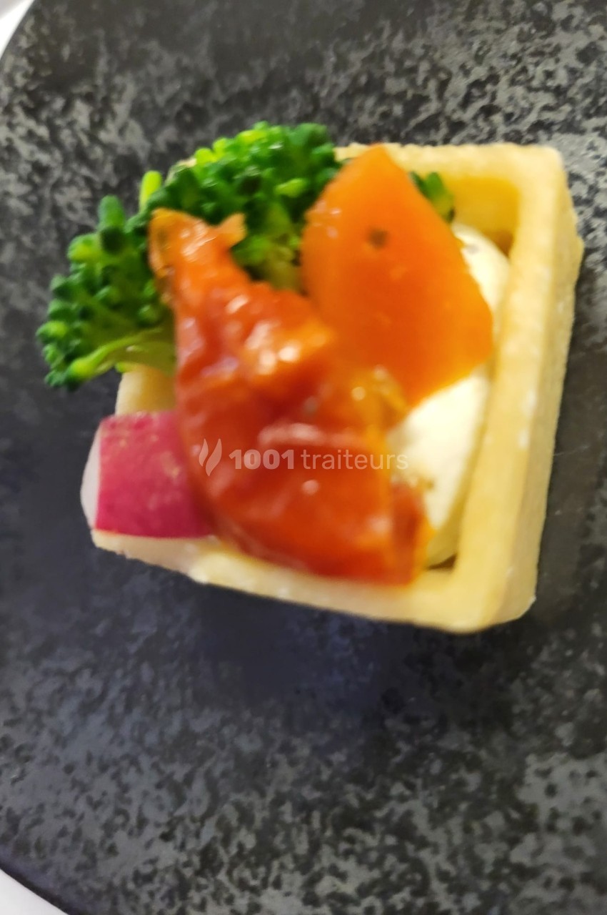 Tartelette garnie de légumes colorés, brocoli, tomate et fromage, présentée sur une assiette noire.