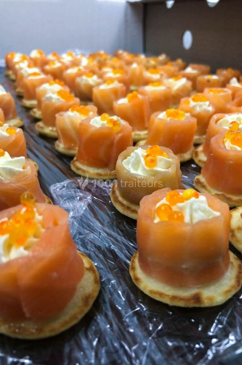 Bouchées apéritives composées de saumon fumé, crème et œufs de poisson sur des blinis disposés en rangées.
