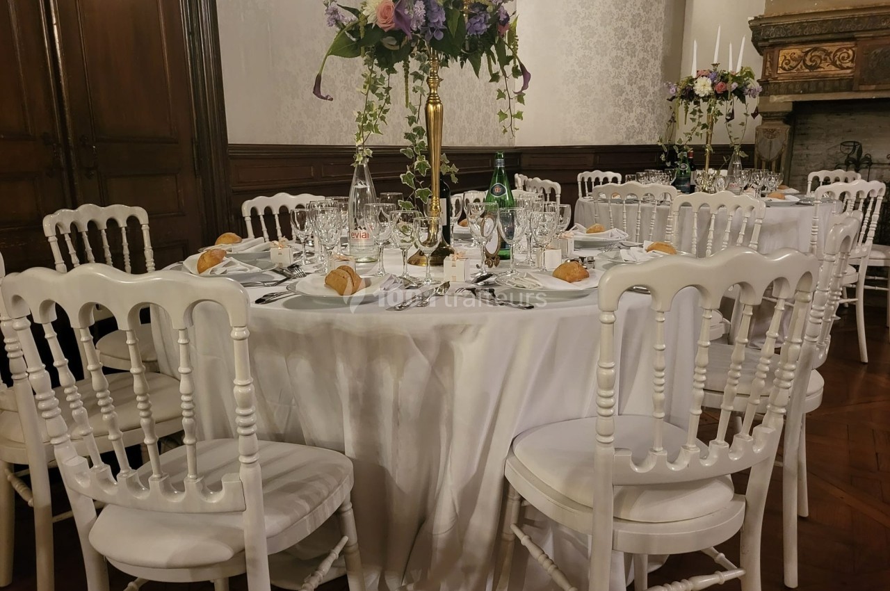 Table ronde élégamment dressée avec nappes blanches, chaises assorties, vaisselle raffinée et centre de table fleuri.