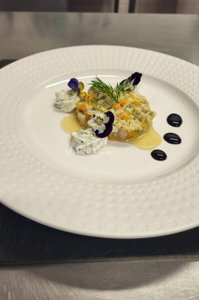 Assiette de tartare de poisson décorée de fleurs comestibles, herbes fraîches et sauces disposées avec précision.