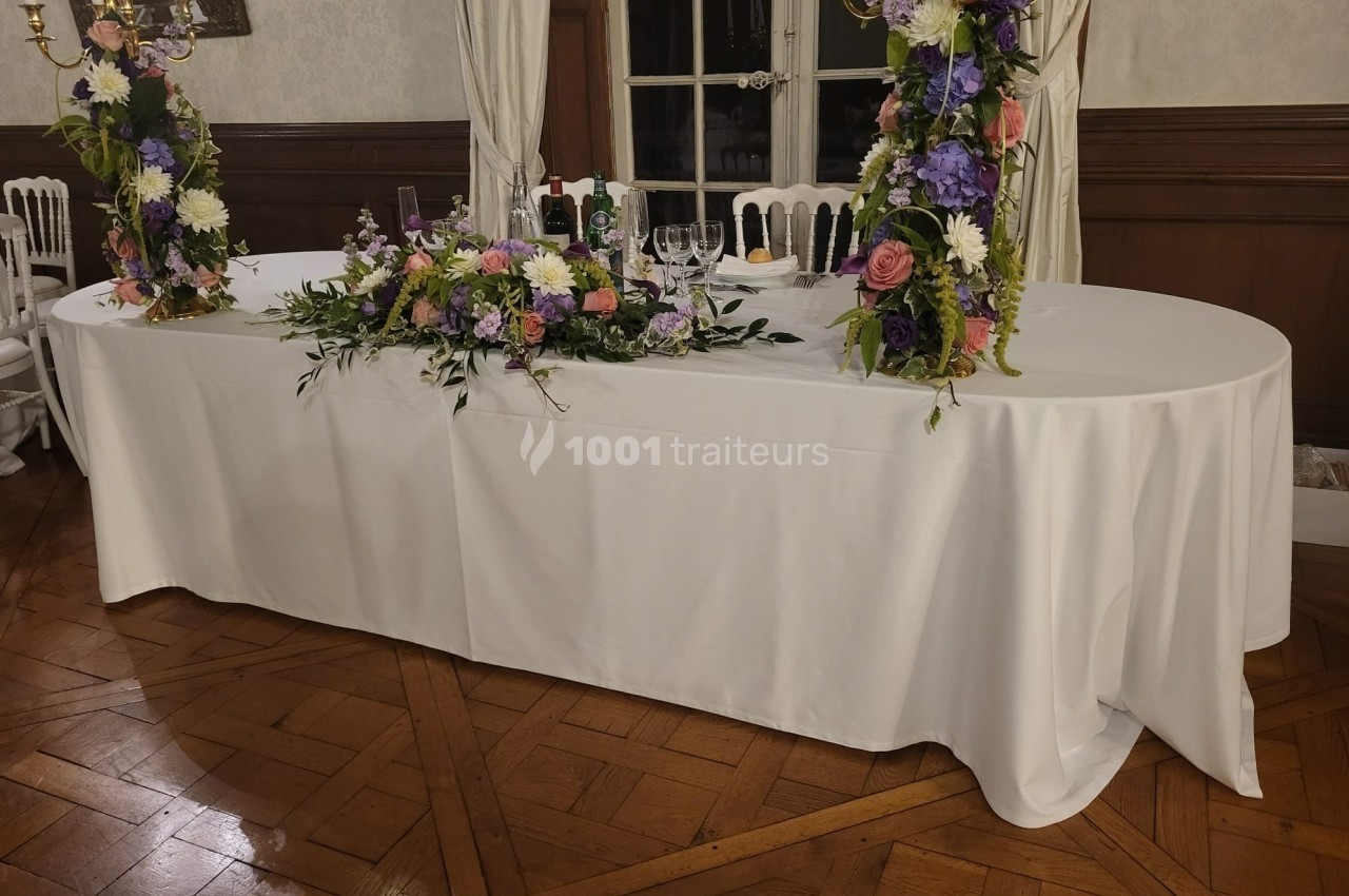 Table ovale recouverte d'une nappe blanche, décorée de compositions florales colorées et de chandeliers dorés.