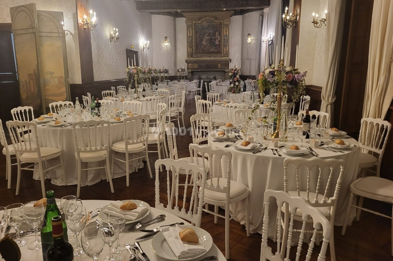 Salle de réception élégante avec tables rondes dressées, décor floral et chaises blanches.