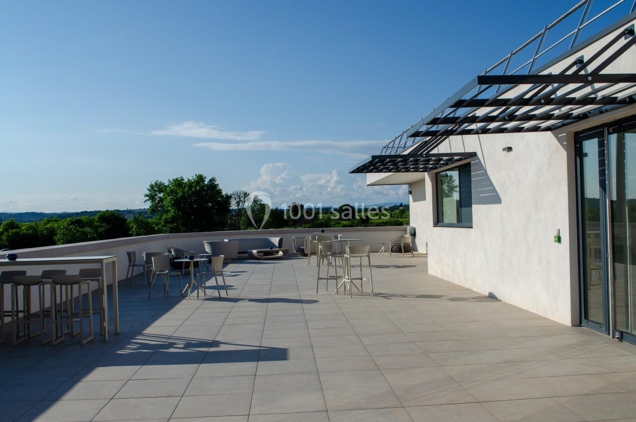 Terrasse spacieuse avec mobilier moderne, vue dégagée sur un paysage verdoyant sous un ciel bleu clair.
