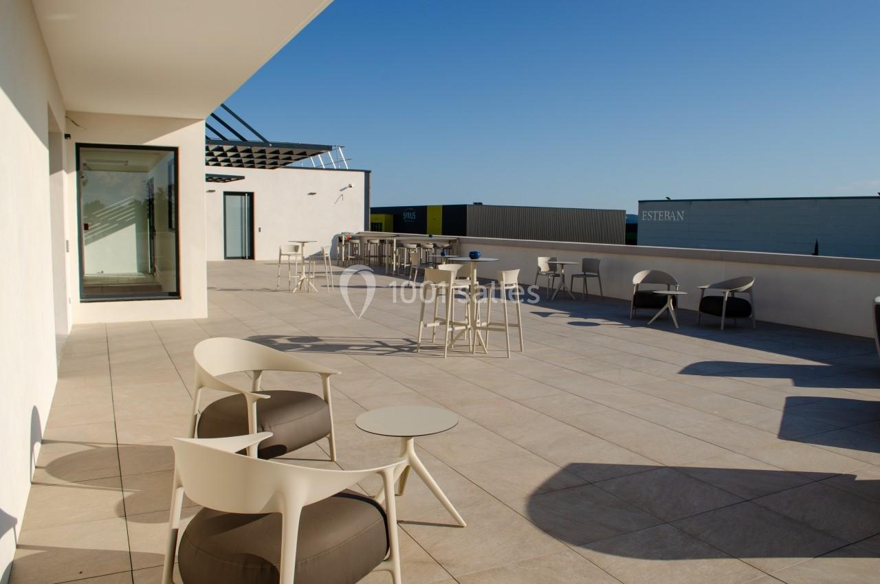 Terrasse spacieuse avec mobilier moderne, tables et chaises, sous un ciel dégagé en fin de journée.