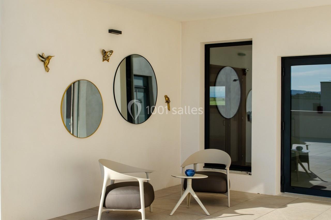 Deux fauteuils modernes et une table basse sur une terrasse, avec des miroirs ronds et des décorations murales.