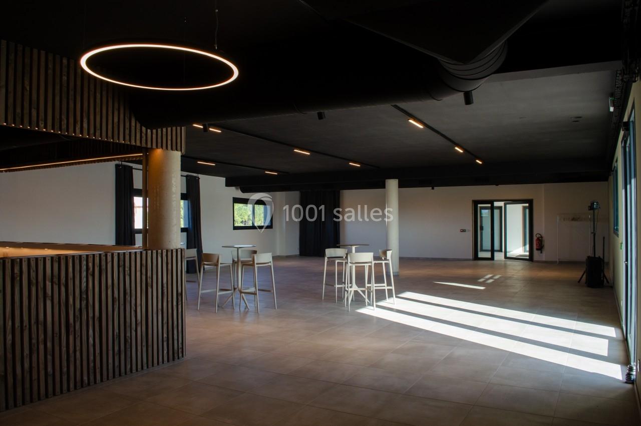 Salle spacieuse avec un éclairage moderne, des tables hautes et un sol carrelé, baignée de lumière naturelle.