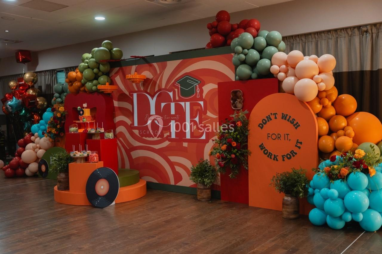 Décor festif coloré avec ballons, fleurs et panneaux, incluant un message motivant et un thème scolaire.