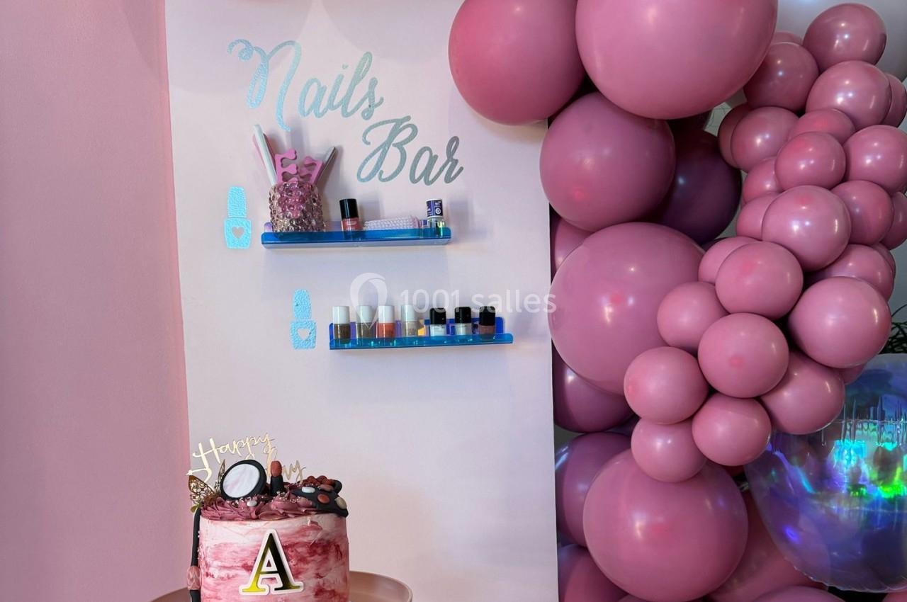 Mur décoré avec des étagères de vernis à ongles, ballons roses et un gâteau d'anniversaire sur une table.
