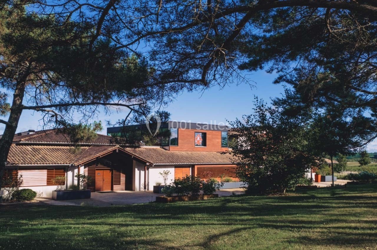 Bâtiment moderne entouré d'arbres, avec une façade en bois et un ciel dégagé en arrière-plan.