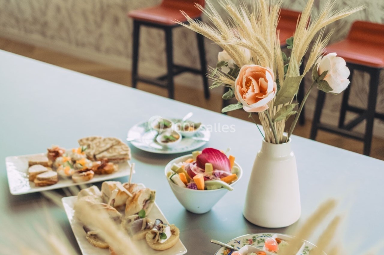 Assortiment de plats et d'amuse-bouches disposés sur une table, avec un vase de fleurs en arrière-plan.