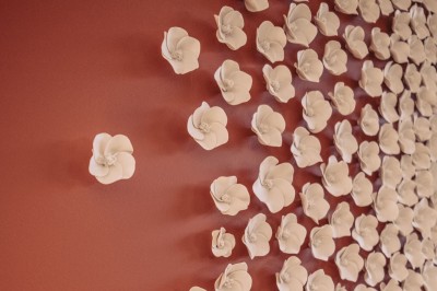 Fleurs blanches en céramique fixées sur un mur rouge, formant une composition artistique.