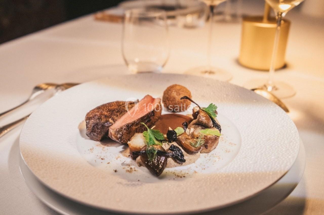Assiette gastronomique avec viande grillée, légumes rôtis, croquette et sauce, servie sur une table élégamment dressée.
