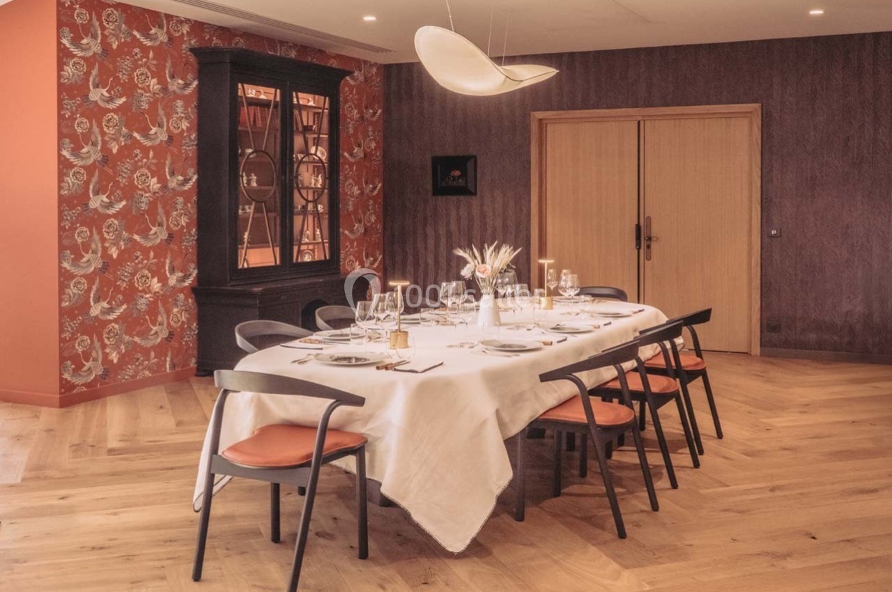 Salle à manger élégante avec une grande table dressée, chaises noires et mur décoré de motifs floraux rouges.
