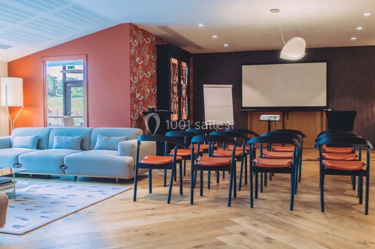 Salle de réunion lumineuse avec chaises alignées, canapé, écran de projection et tableau blanc.