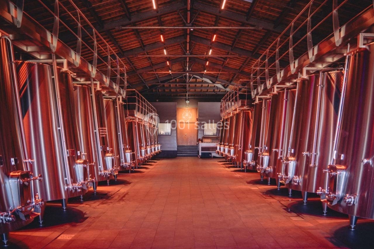 Salle avec de grandes cuves en inox alignées sous un toit en bois, éclairée par une lumière rouge tamisée.