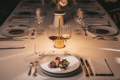 Vue aérienne d'une terrasse animée entourée de vignes au coucher du soleil, avec des invités profitant du cadre.