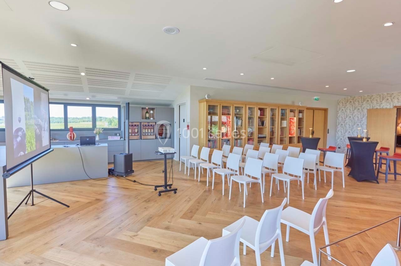 Salle lumineuse aménagée pour une présentation, avec des chaises alignées, un écran de projection et un mobilier moderne.