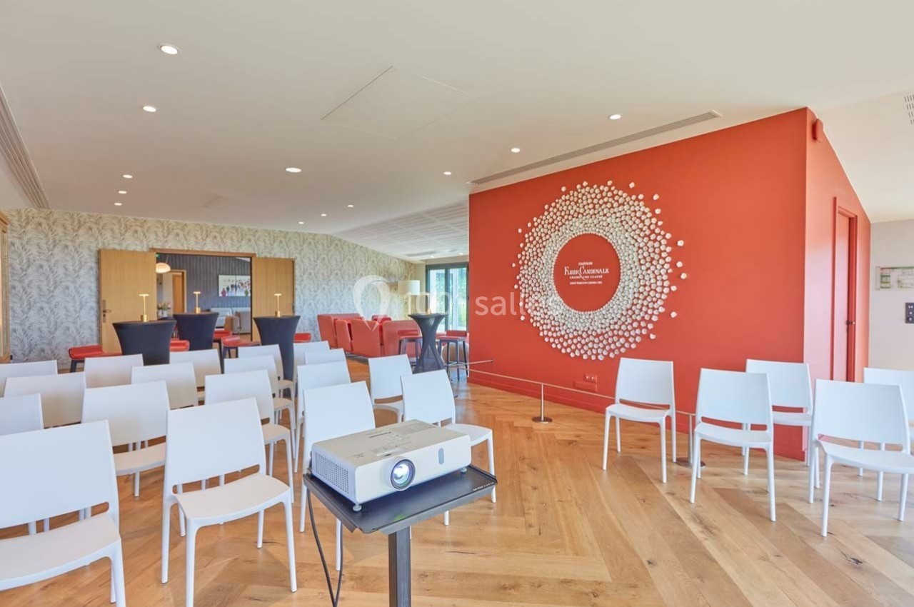 Salle de conférence lumineuse avec chaises blanches, projecteur et mur rouge décoré d'un motif circulaire.
