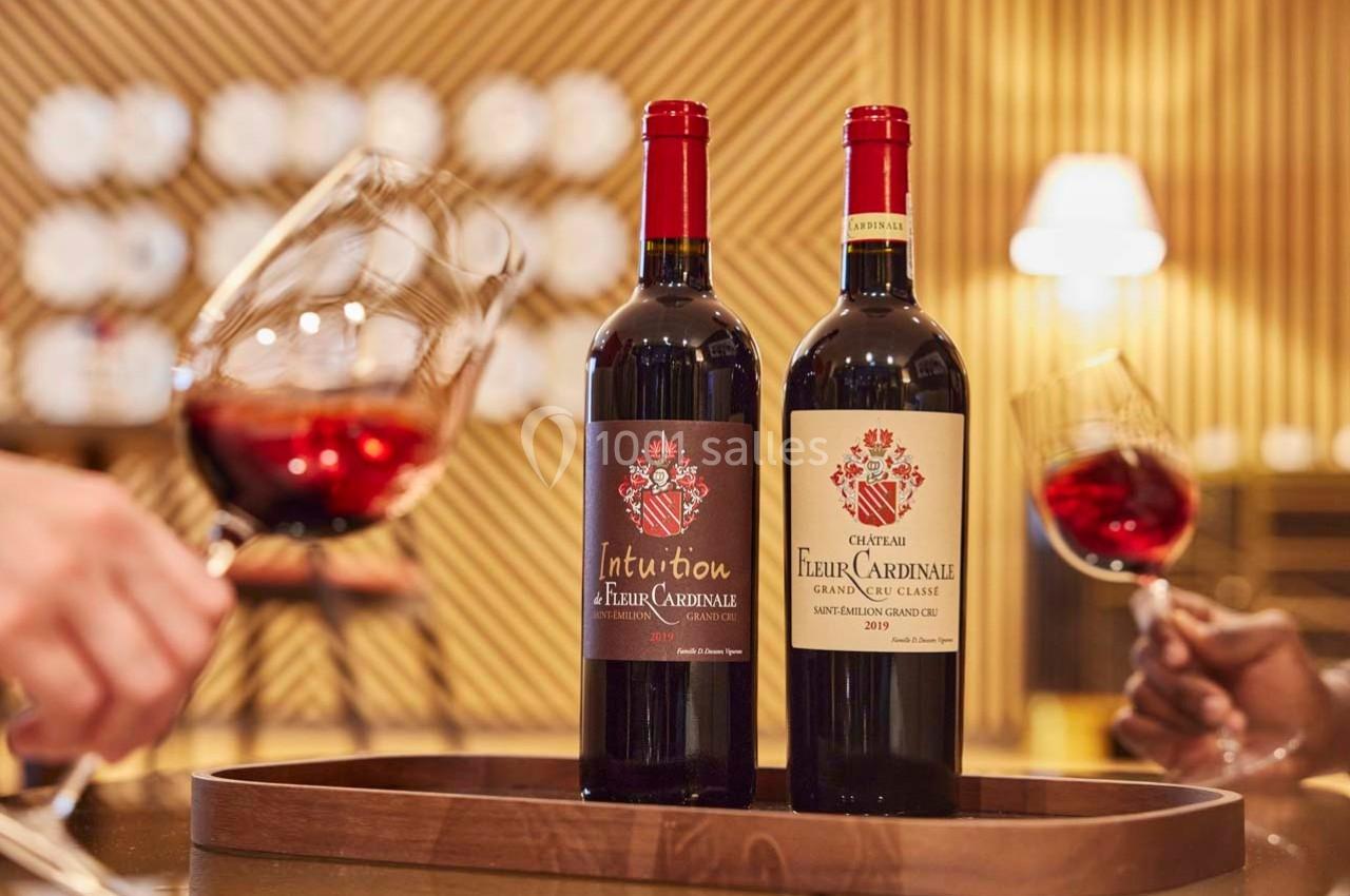 Deux bouteilles de vin rouge sur un plateau en bois, entourées de verres de vin dans un cadre chaleureux.