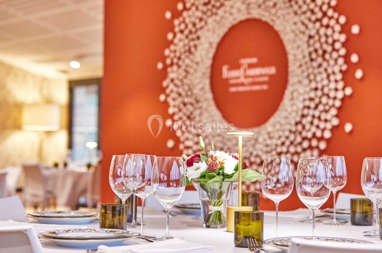 Salle de restaurant élégante avec tables dressées, décorée d'un mur rouge orné d'une œuvre circulaire en relief.
