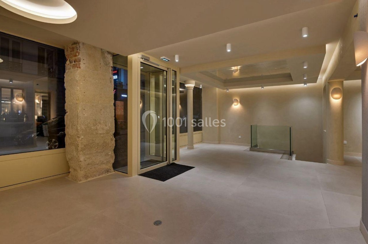 Entrée moderne avec sol en carrelage clair, murs beige, éclairage encastré et porte vitrée automatique.