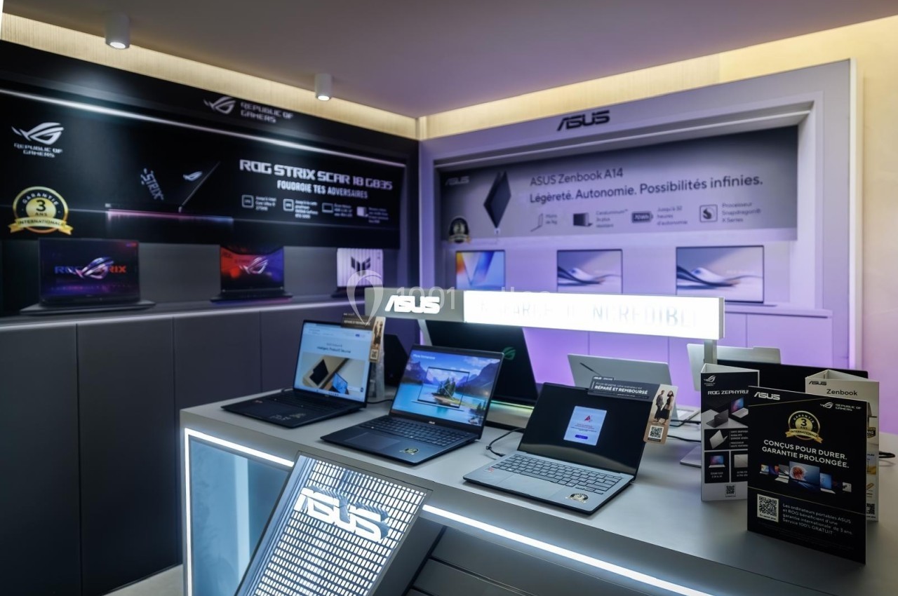 Ordinateurs portables exposés sur un présentoir dans un magasin, avec des affiches promotionnelles en arrière-plan.