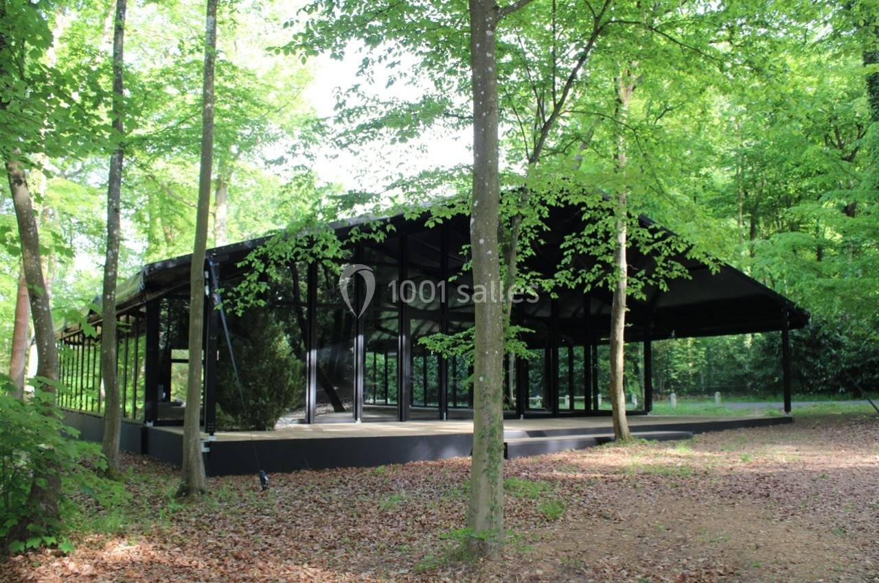 Pavillon moderne en verre et métal entouré d'arbres dans une forêt verdoyante.