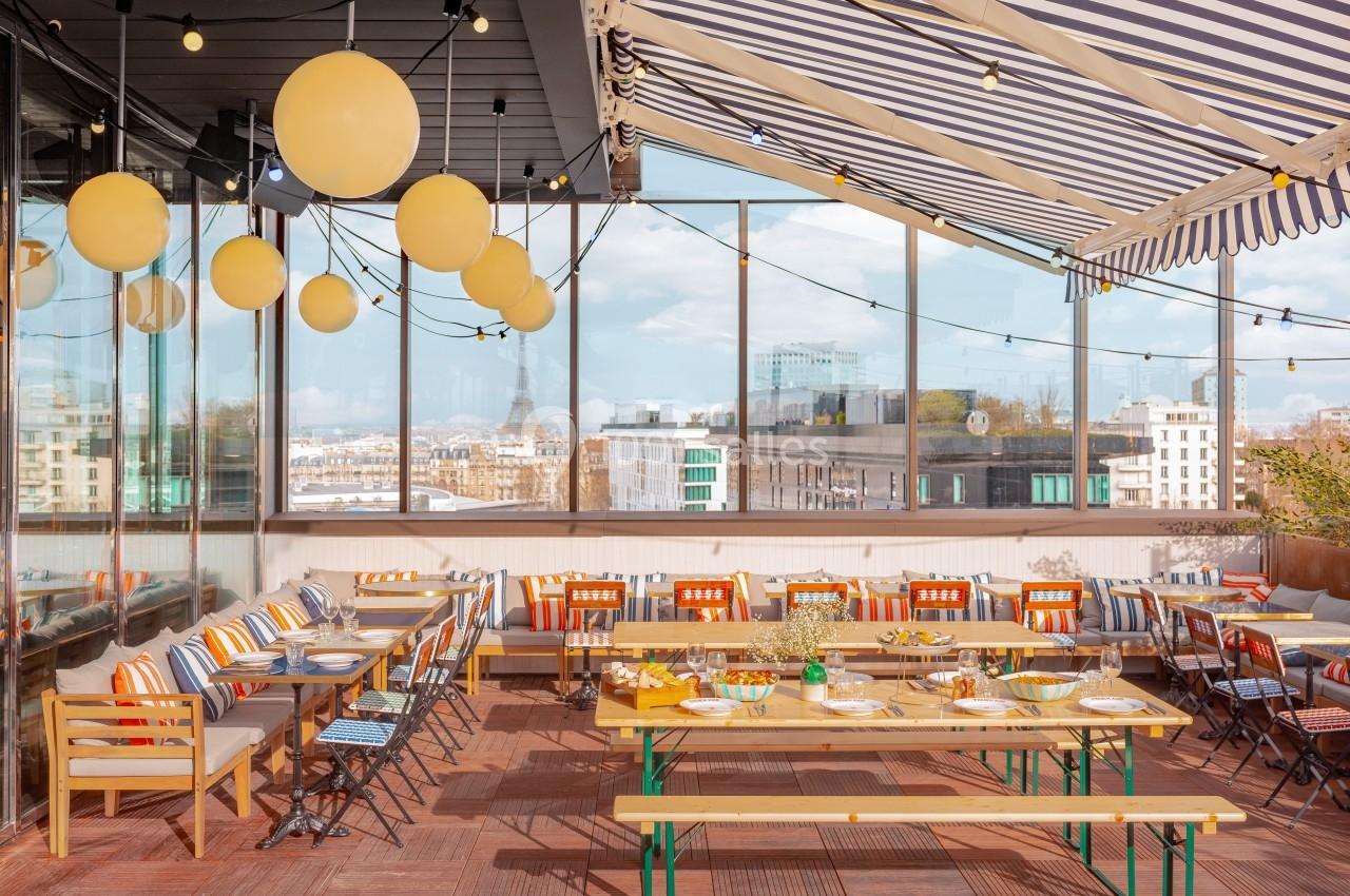 Terrasse aménagée avec des tables dressées, des chaises colorées et des lampions suspendus sous une pergola rayée.