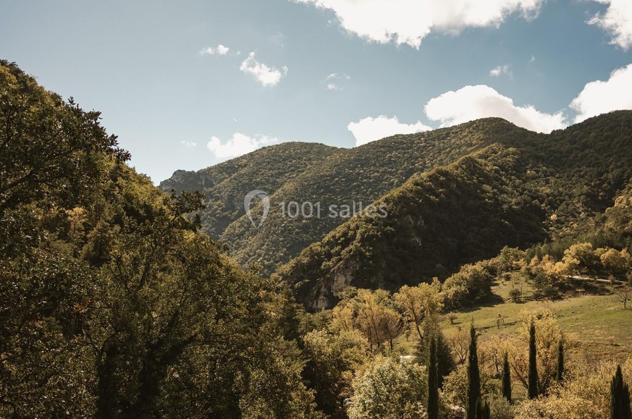 Paysage vallonné avec collines boisées, ciel partiellement nuageux et végétation méditerranéenne au premier plan.