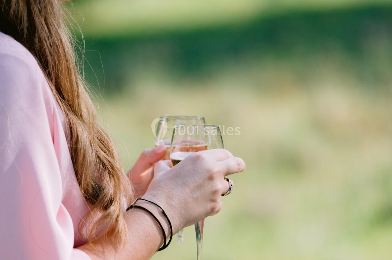 Une femme en robe rose tient un verre de vin blanc dans un jardin ensoleillé.
