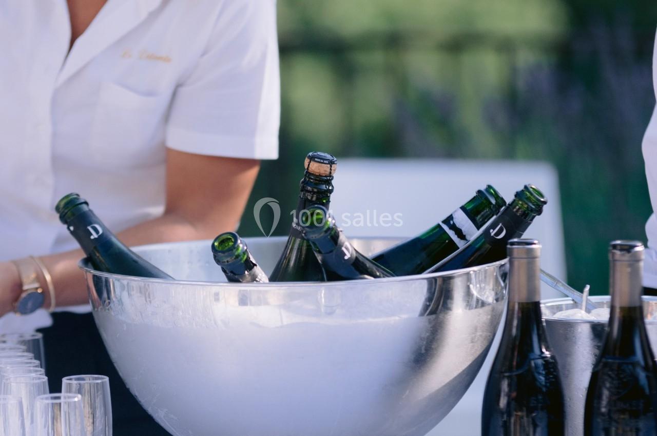 Une femme en chemise blanche prépare une table avec un seau rempli de bouteilles et des verres à champagne.