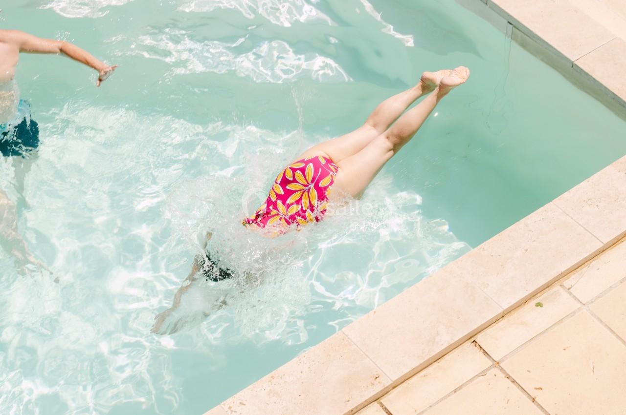 Une personne plonge dans une piscine, créant des éclaboussures, avec un maillot à motifs colorés.