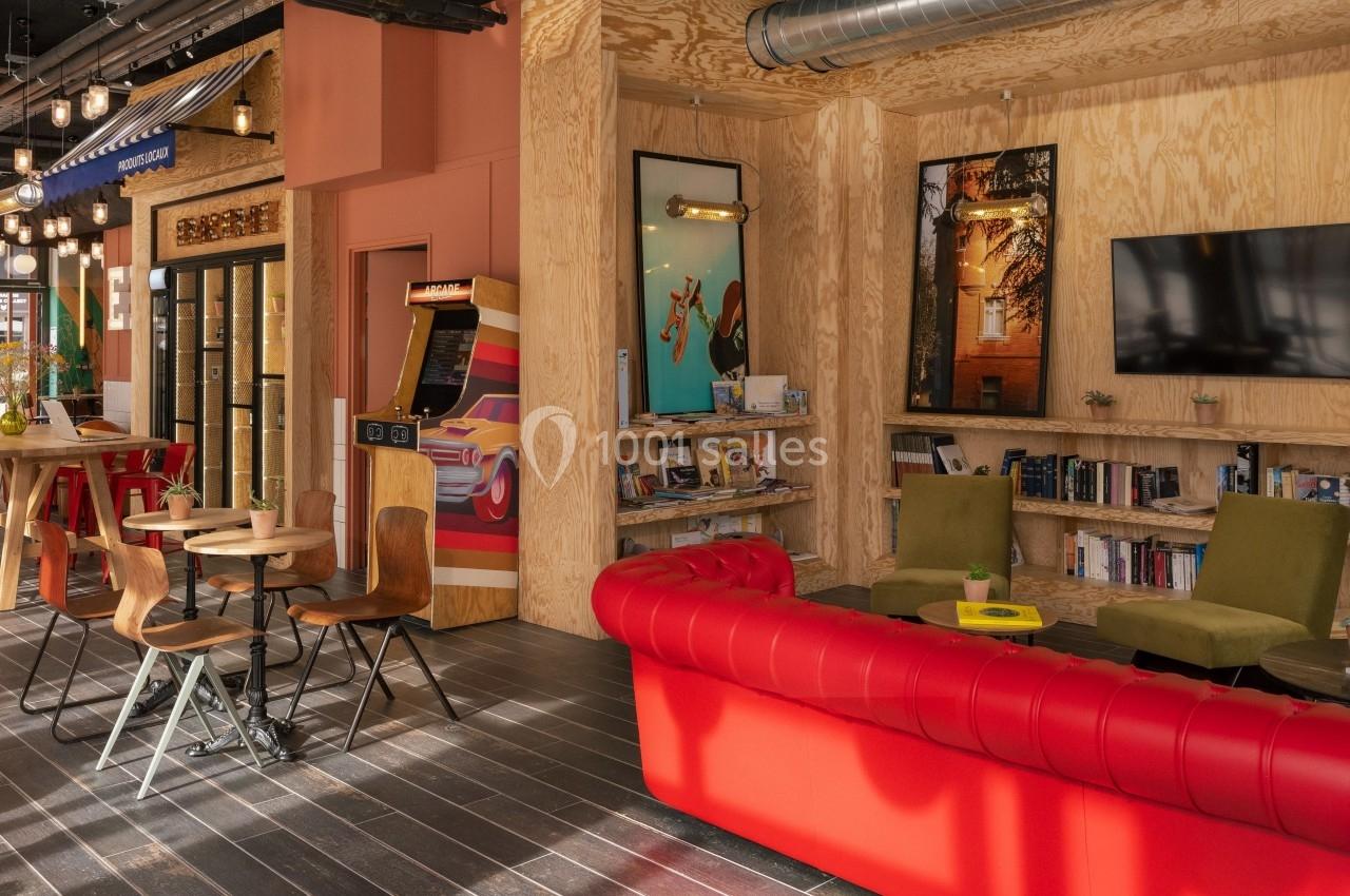 Espace intérieur chaleureux avec canapé rouge, étagères remplies de livres, tables, chaises et décorations lumineuses.