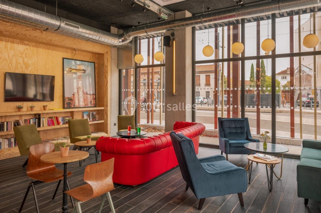 Espace lounge lumineux avec canapés, fauteuils colorés, tables en bois et grande baie vitrée donnant sur l'extérieur.