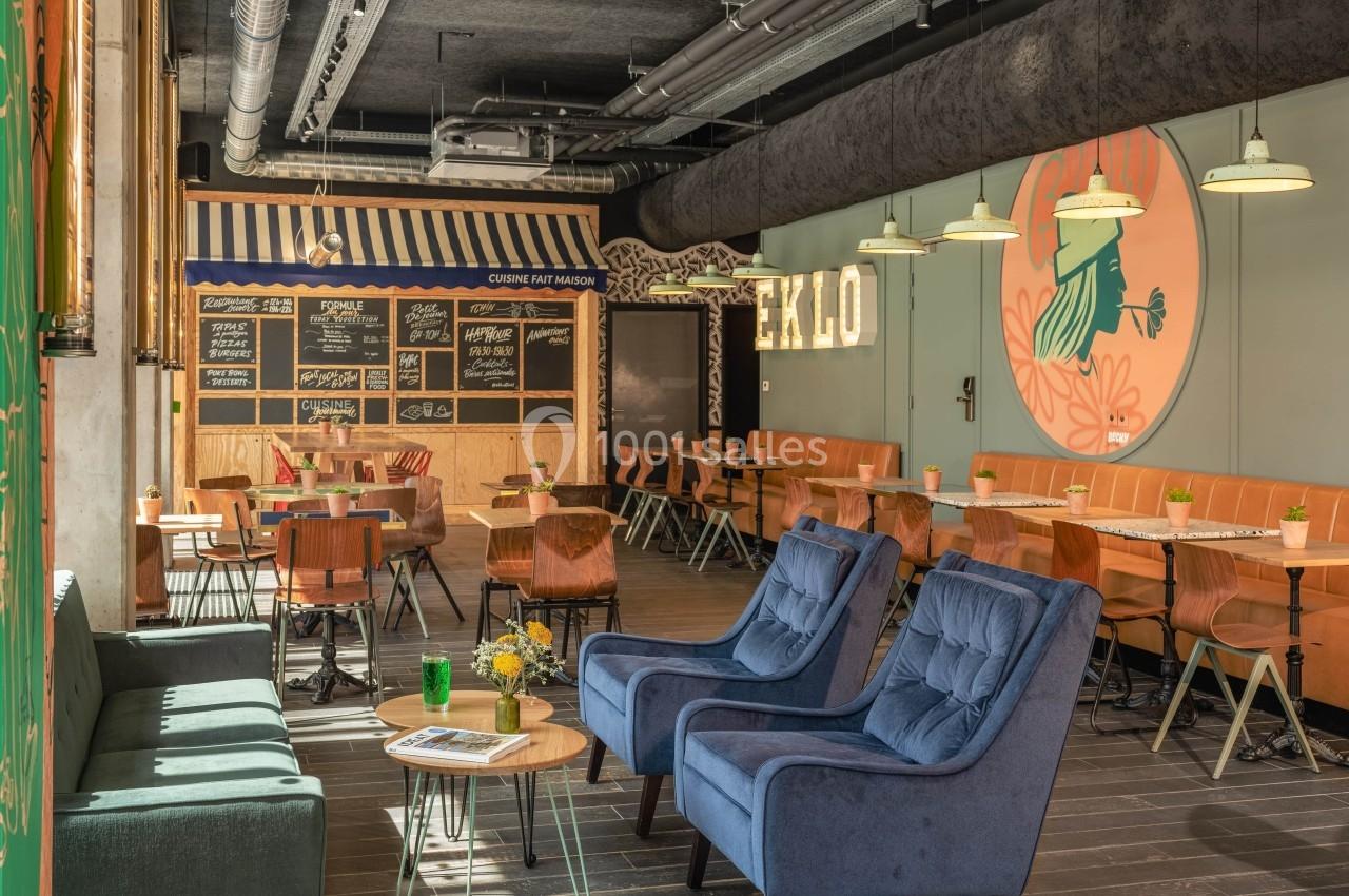 Salle de restaurant moderne avec mobilier coloré, tableaux noirs au mur et ambiance lumineuse chaleureuse.