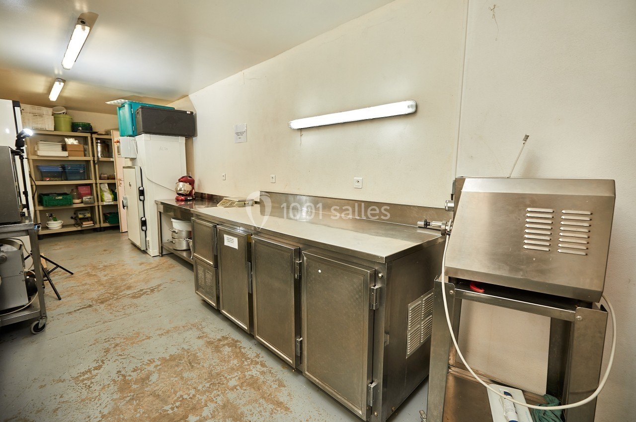Cuisine professionnelle avec plans de travail en inox, réfrigérateurs, étagères de rangement et éclairage fluorescent.