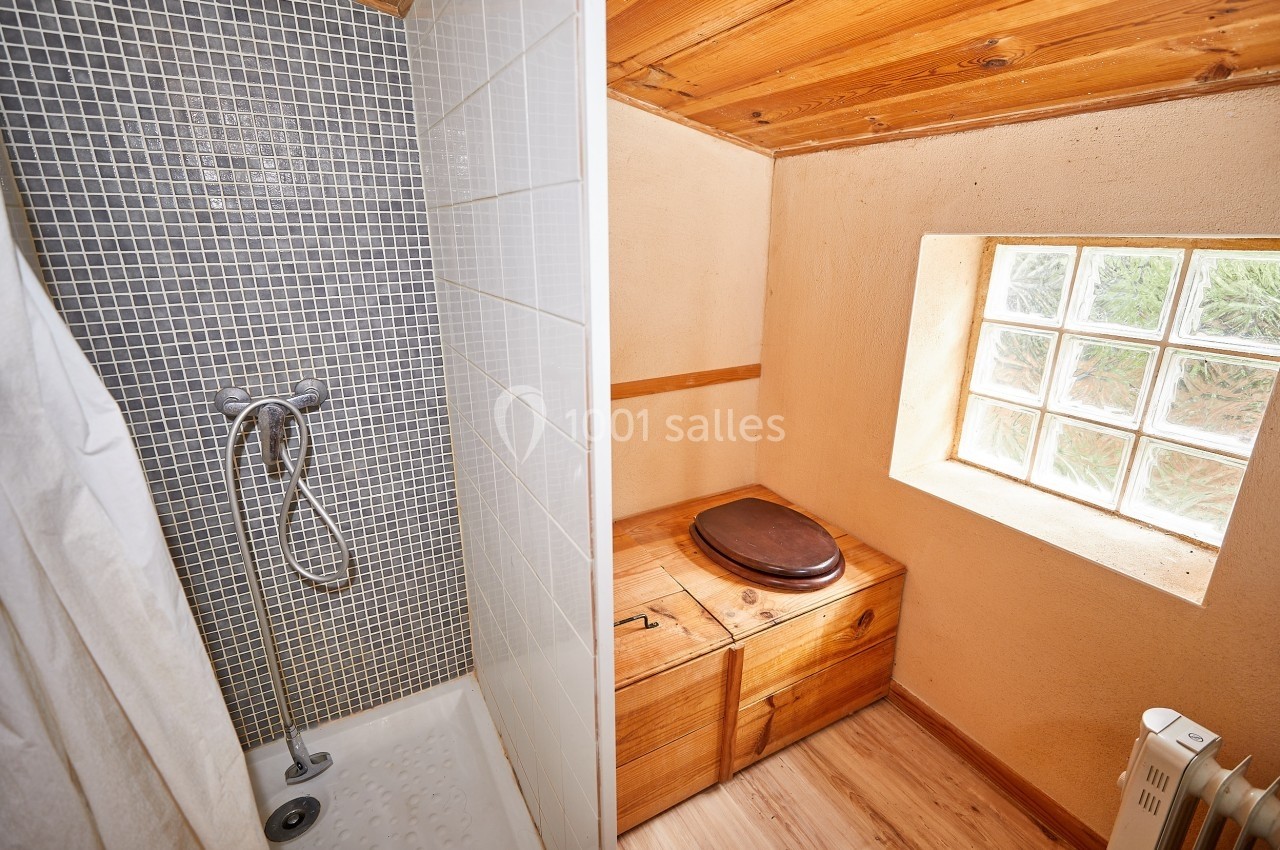 Douche avec carrelage gris à gauche et toilettes en bois près d'une fenêtre en pavés de verre à droite.