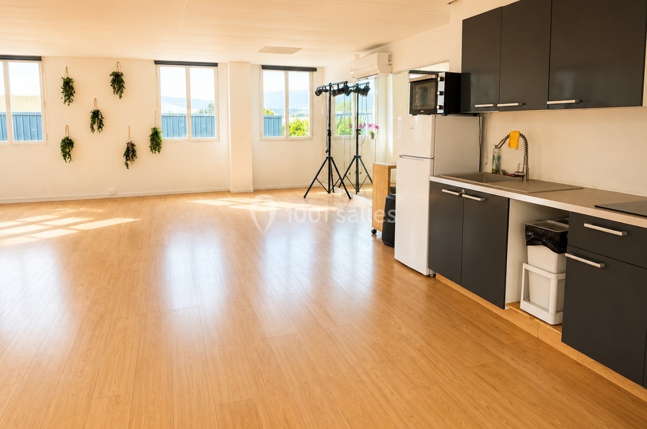 Cuisine ouverte moderne avec meubles noirs, sol en parquet clair, grande pièce lumineuse et plantes murales décoratives.
