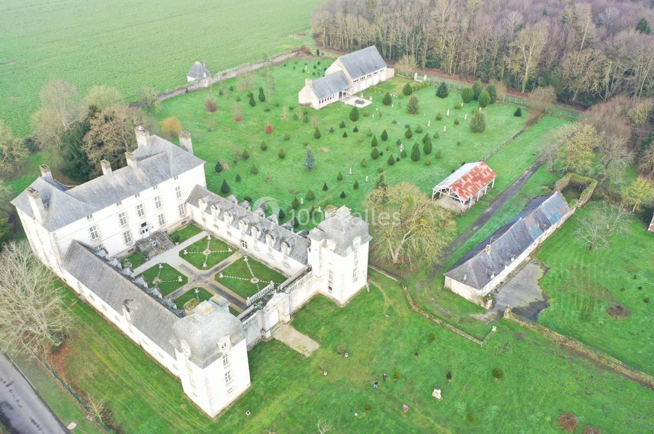 Vue aérienne d'un château entouré de jardins, de bâtiments annexes et de prairies verdoyantes.