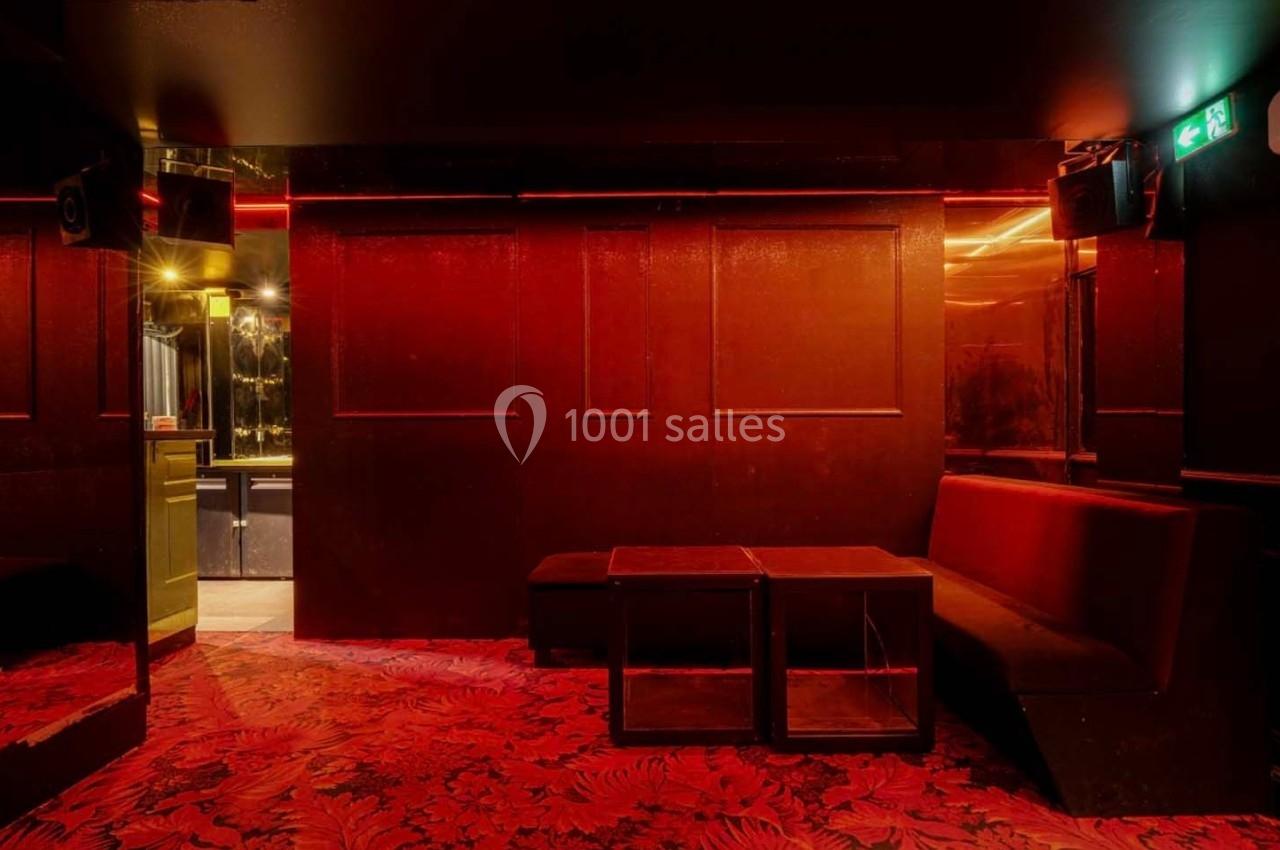 Salle sombre avec murs rouges, banquettes assorties, tables basses et éclairage tamisé, ambiance intime.
